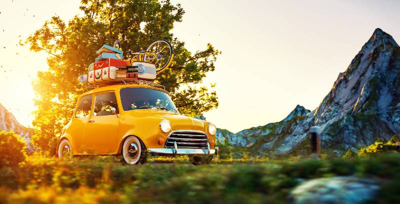 Une jolie petite voiture rétro avec des valises et un vélo sur le dessus passe par un magnifique camping de voiture de campagne
