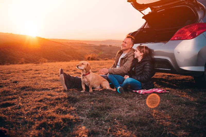 Père et fille avec un petit chien jaune campant sur une colline alors qu'ils étaient assis par terre près de la voiture-voiture camping