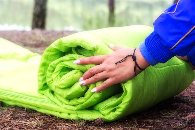 Une femme plie et emballe un sac de couchage-Tente de lit de camion