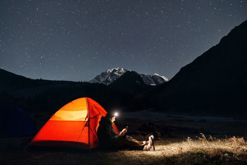 Lampe frontale homme près de la tente orange rougeoyante | Phares