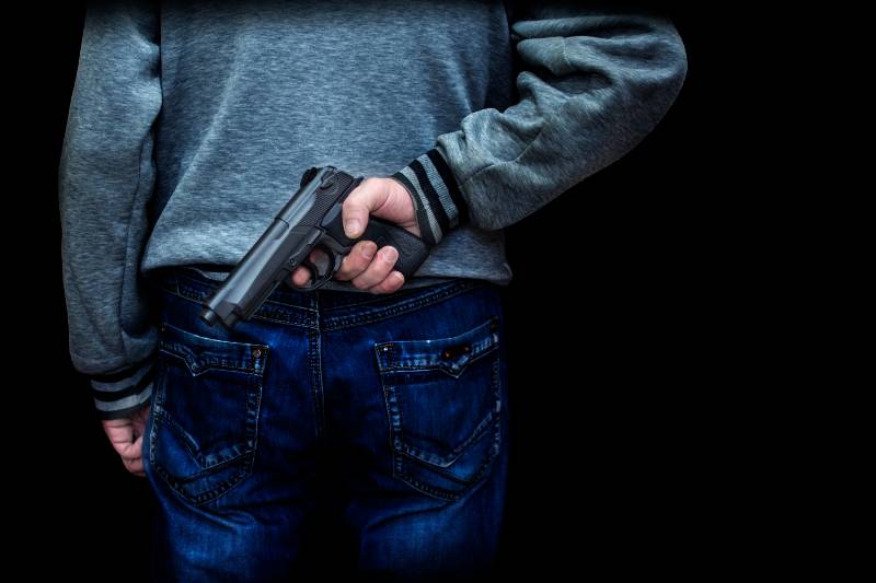 homme tenant une arme dans le dos sur un fond noir | Tir de masse